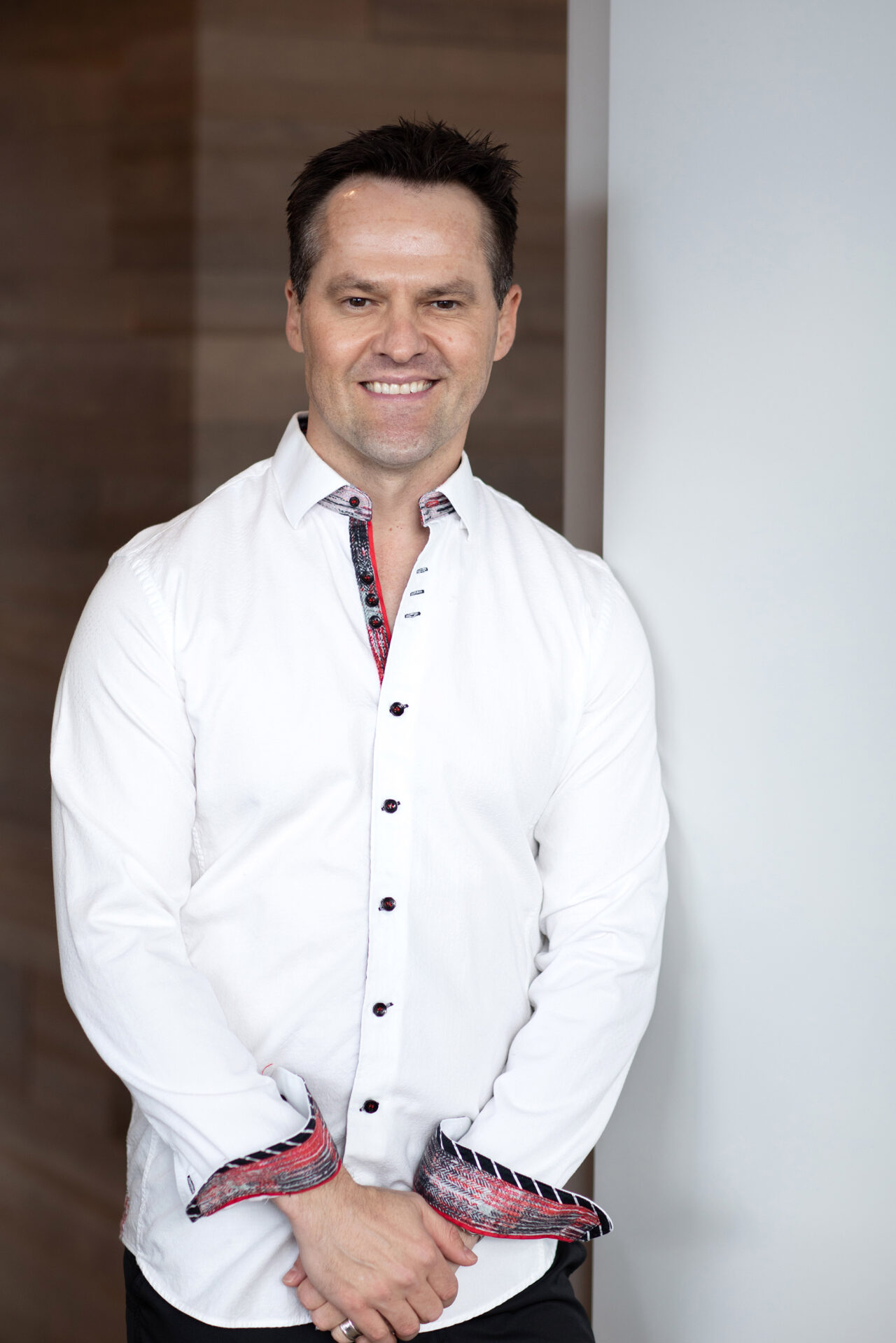 An image of Dr Ben Wiese in a white button-up shirt standing next to a white wall. 